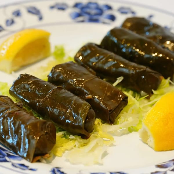 Greek dolmades, grape leaves stuffed with rice, served on lettuce with lemon wedges.
