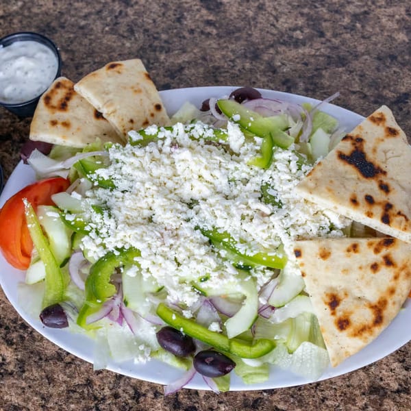 A fresh Greek salad with feta, olives, bell peppers, and pita bread on a white plate.