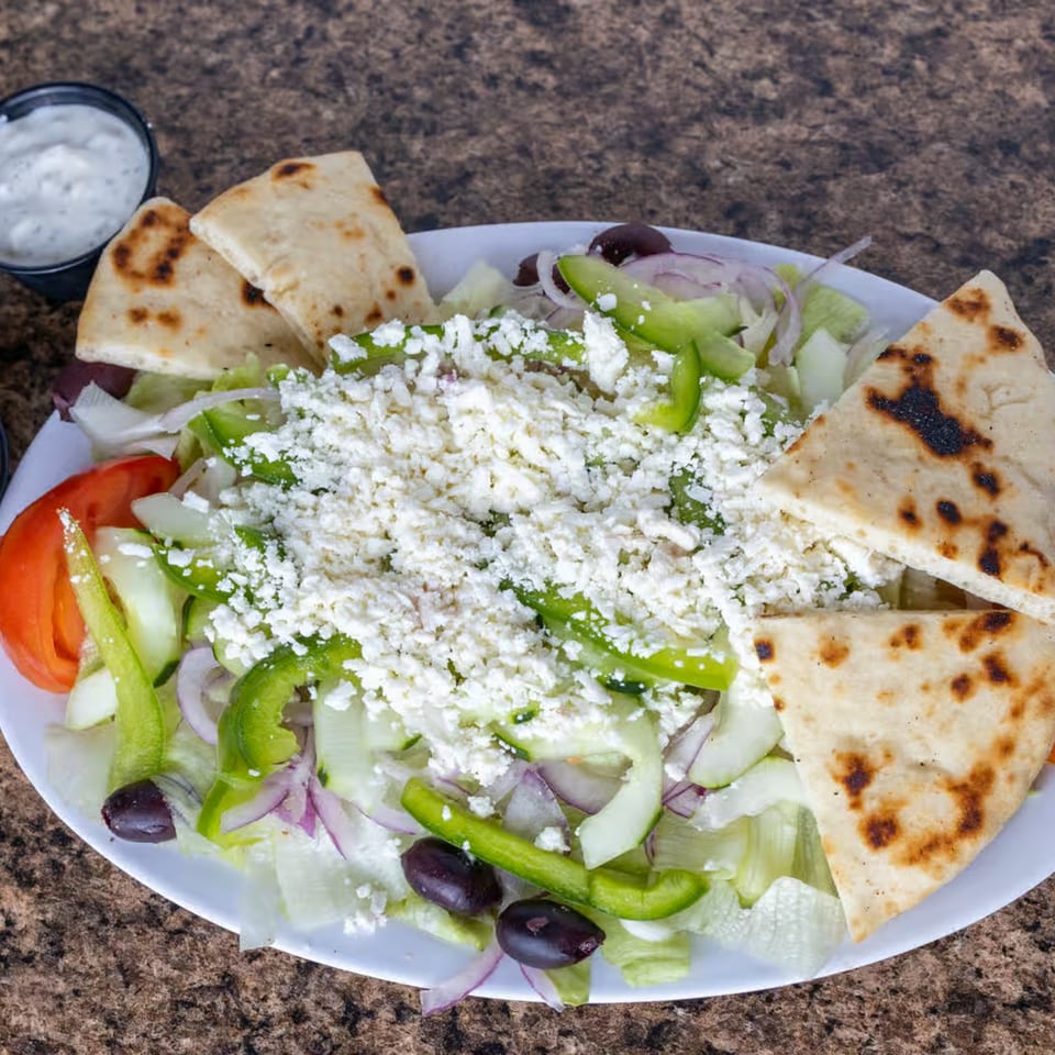 A fresh Greek salad with feta, olives, bell peppers, and pita bread on a white plate.