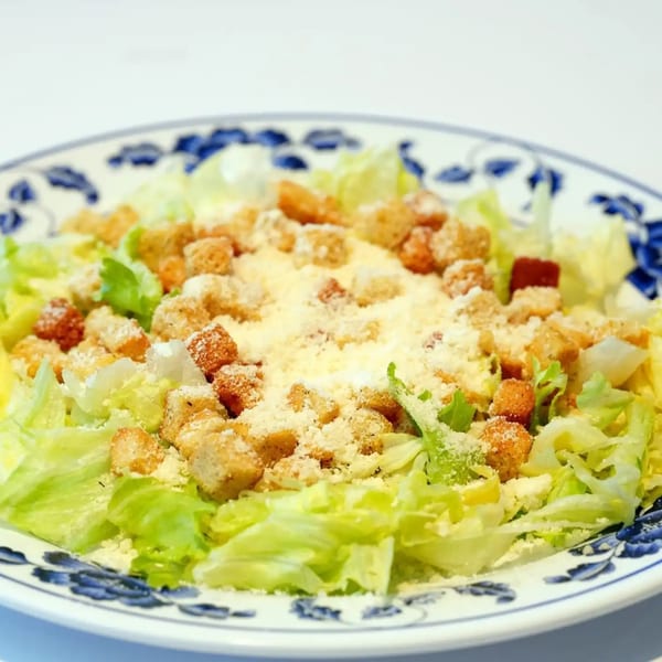 A fresh Caesar salad with crisp lettuce, golden croutons, and grated cheese on a decorative plate.