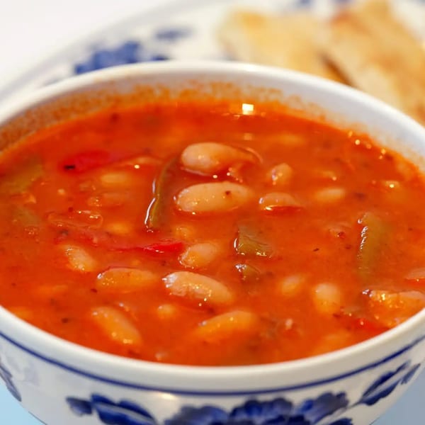A white bowl with blue floral patterns filled with a rich red bean soup, served with bread.